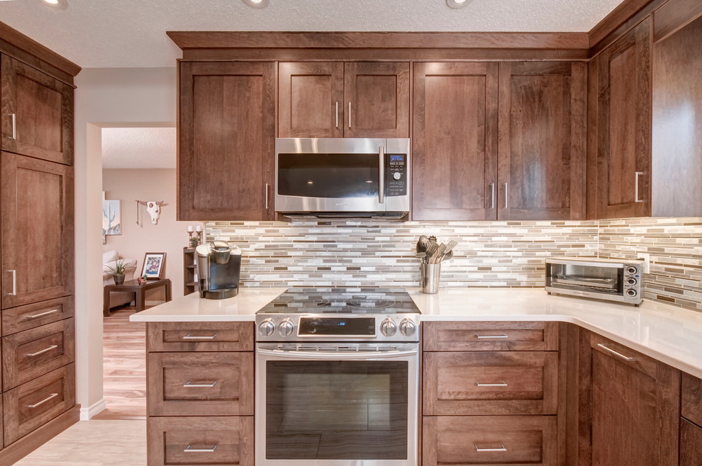 Mid-sized transitional l-shaped porcelain tile and beige floor eat-in kitchen photo in Calgary with an undermount sink, shaker cabinets, medium tone wood cabinets, quartz countertops, multicolored backsplash, mosaic tile backsplash, stainless steel appliances and no island