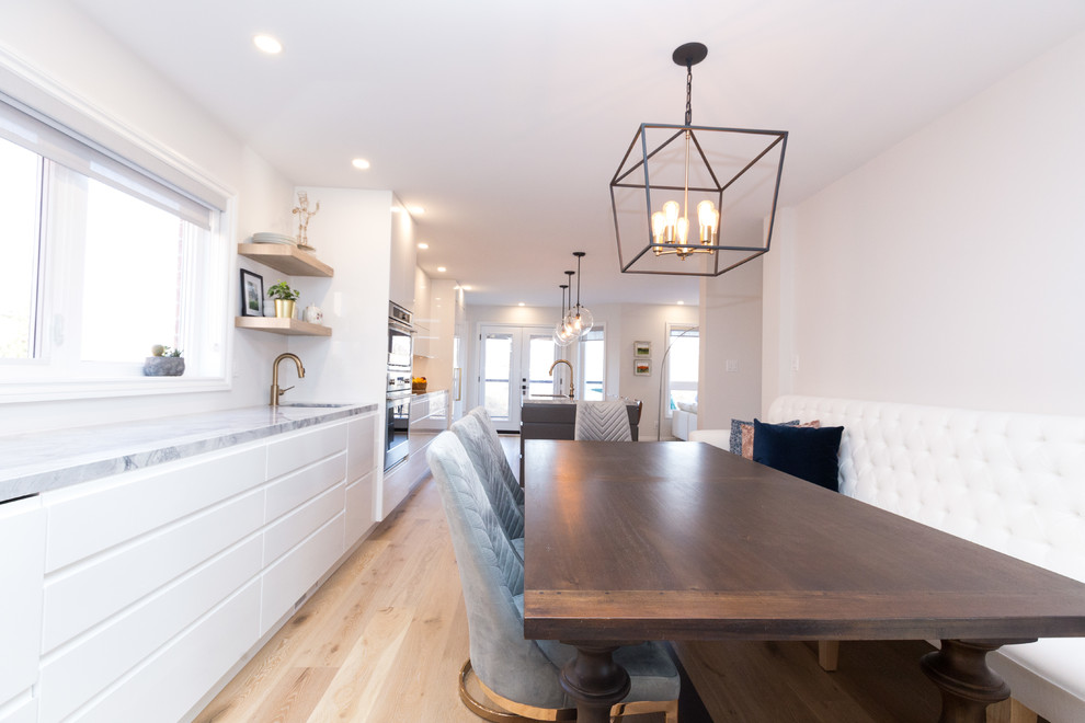 This is an example of a large modern single-wall eat-in kitchen in Toronto with an undermount sink, flat-panel cabinets, white cabinets, quartzite benchtops, white splashback, marble splashback, coloured appliances, light hardwood floors, with island and beige floor.
