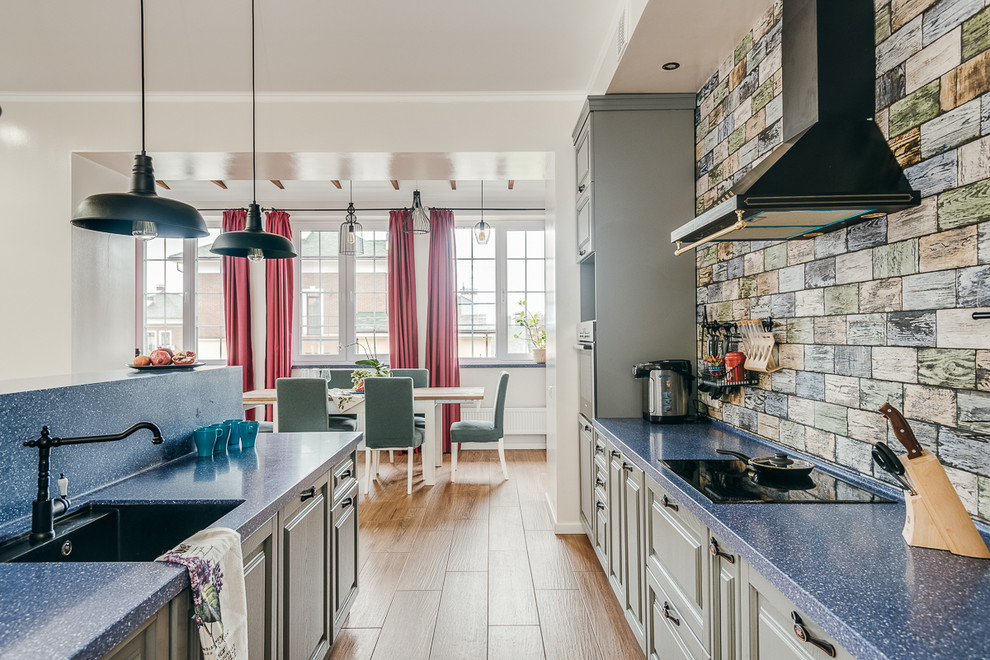 Inspiration for a large country galley eat-in kitchen in Moscow with a farmhouse sink, raised-panel cabinets, blue cabinets, multi-coloured splashback, ceramic splashback, panelled appliances, porcelain floors, with island, brown floor and blue benchtop.