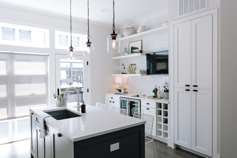 Example of a mid-sized transitional galley dark wood floor and gray floor enclosed kitchen design in DC Metro with an undermount sink, recessed-panel cabinets, white cabinets, solid surface countertops, stainless steel appliances, an island, white countertops, white backsplash and subway tile backsplash