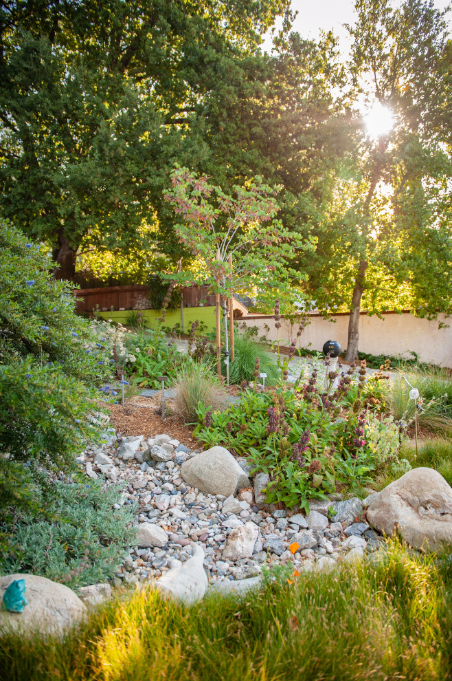 Large country front yard partial sun xeriscape in Los Angeles with a garden path, river rock and a wood fence for spring.