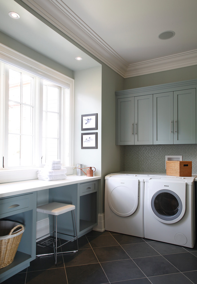 Mid-sized traditional l-shaped utility room in Toronto with blue cabinets, shaker cabinets, solid surface benchtops, ceramic floors, a side-by-side washer and dryer, grey floor, white benchtop and grey walls.