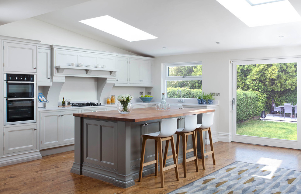 Inspiration for a large transitional l-shaped open plan kitchen in Dublin with a farmhouse sink, beaded inset cabinets, grey cabinets, quartzite benchtops, grey splashback, stone slab splashback, stainless steel appliances, medium hardwood floors, with island and brown floor.