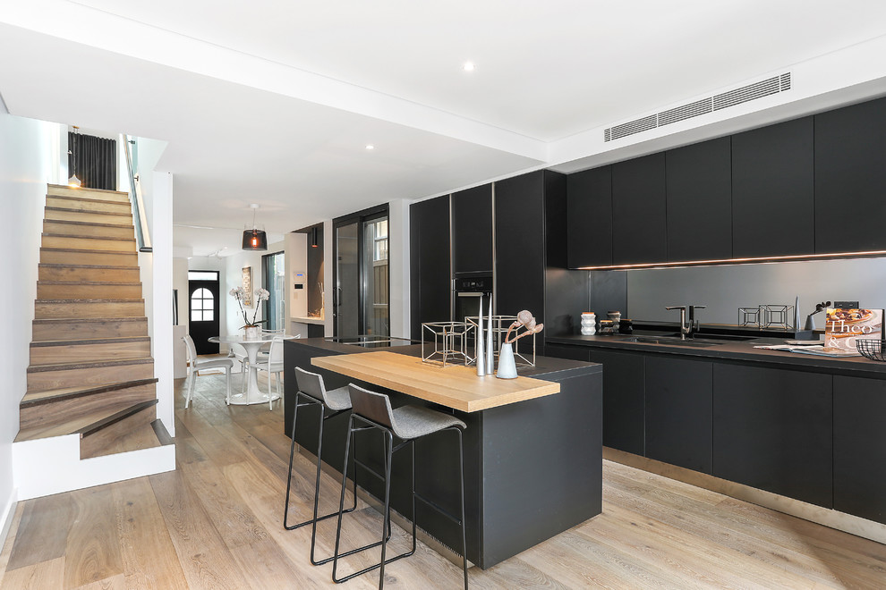 Design ideas for a small contemporary single-wall separate kitchen in Sydney with a single-bowl sink, flat-panel cabinets, black cabinets, quartz benchtops, grey splashback, mirror splashback, black appliances, medium hardwood floors, with island, brown floor and black benchtop.
