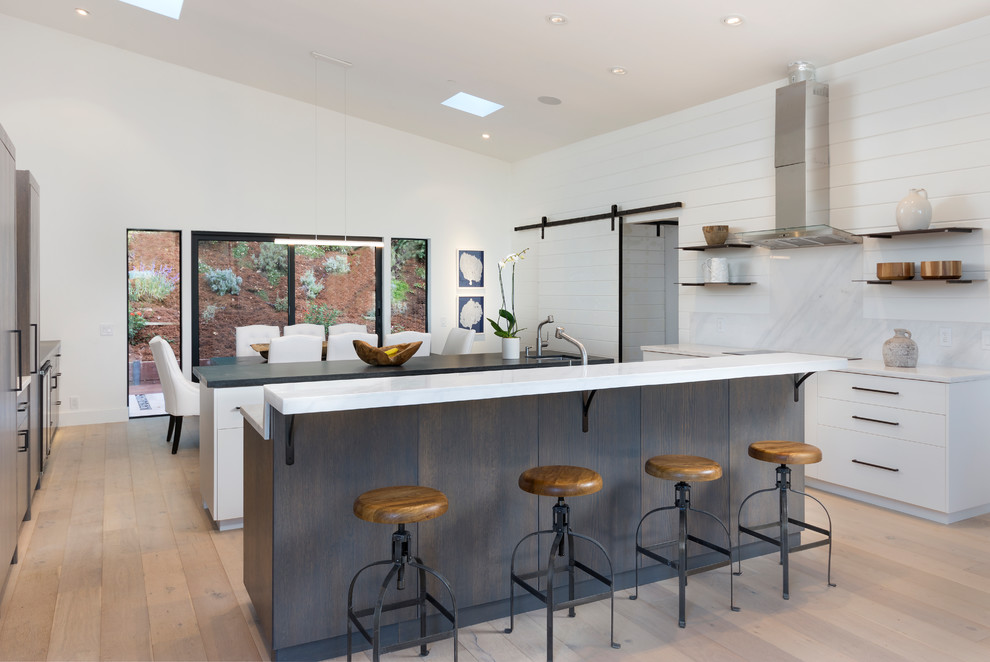 Mid-sized contemporary u-shaped eat-in kitchen in San Francisco with flat-panel cabinets, white cabinets, light hardwood floors, multiple islands, beige floor, white benchtop, quartz benchtops, white splashback, timber splashback and stainless steel appliances.