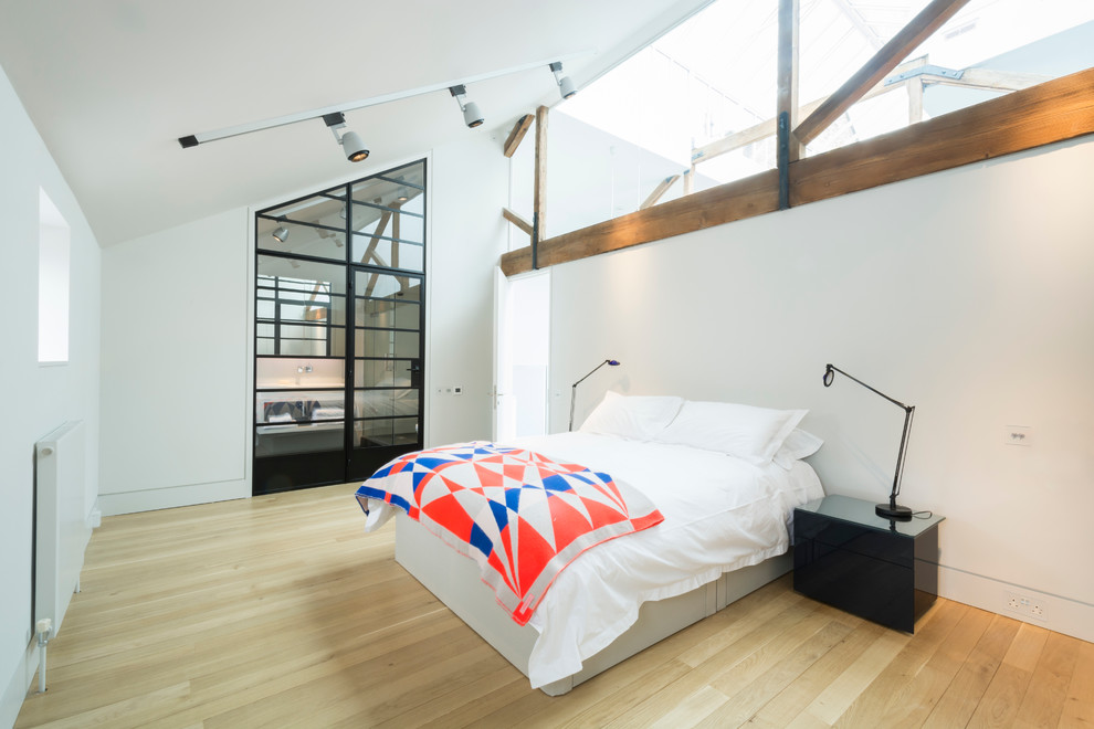 Inspiration for an expansive industrial bedroom in London with white walls and light hardwood floors.