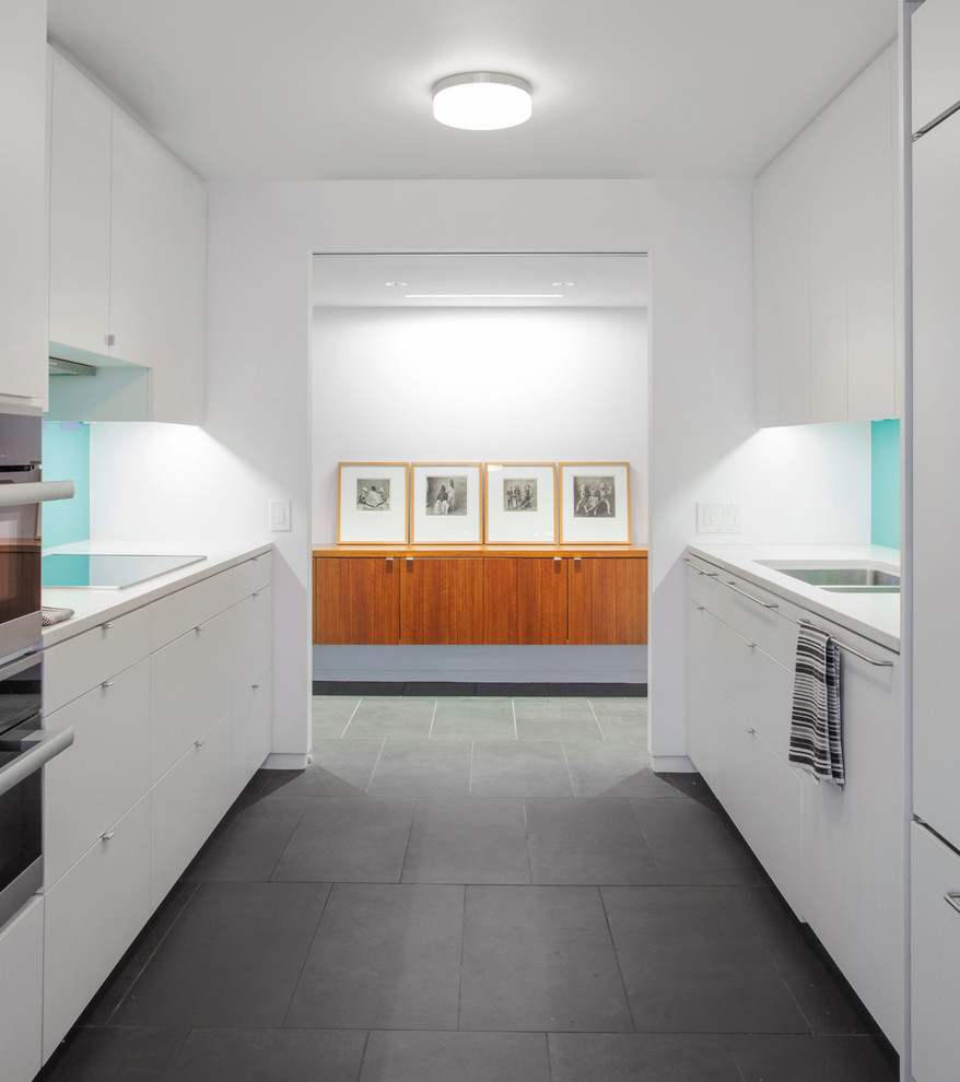 Design ideas for a mid-sized midcentury galley separate kitchen in Chicago with flat-panel cabinets, white cabinets, solid surface benchtops, blue splashback, glass sheet splashback, porcelain floors and no island.