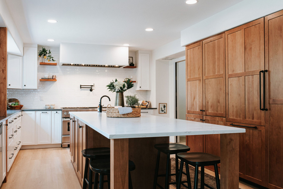 Design ideas for a large country galley eat-in kitchen in Denver with a farmhouse sink, shaker cabinets, white cabinets, granite benchtops, white splashback, subway tile splashback, stainless steel appliances, with island, beige floor, black benchtop and exposed beam.
