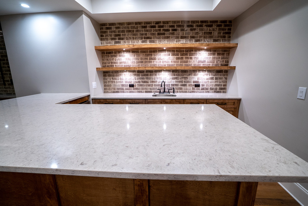 Photo of a mid-sized contemporary l-shaped seated home bar in Atlanta with an undermount sink, shaker cabinets, medium wood cabinets, quartz benchtops, brown splashback, brick splashback, medium hardwood floors, brown floor and beige benchtop.