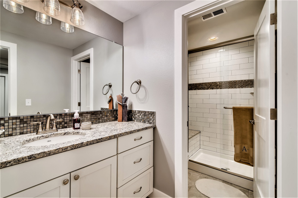 This is an example of a mid-sized country 3/4 bathroom in Denver with shaker cabinets, white cabinets, an alcove shower, a two-piece toilet, multi-coloured tile, mosaic tile, grey walls, ceramic floors, a drop-in sink, quartzite benchtops, grey floor, a sliding shower screen, multi-coloured benchtops, an enclosed toilet, a single vanity and a built-in vanity.