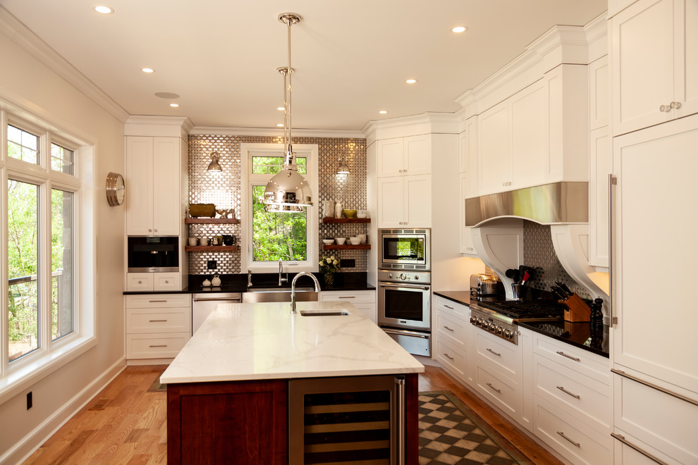 Example of a mid-sized transitional l-shaped enclosed kitchen design with shaker cabinets, white cabinets, stainless steel appliances, an island and white countertops