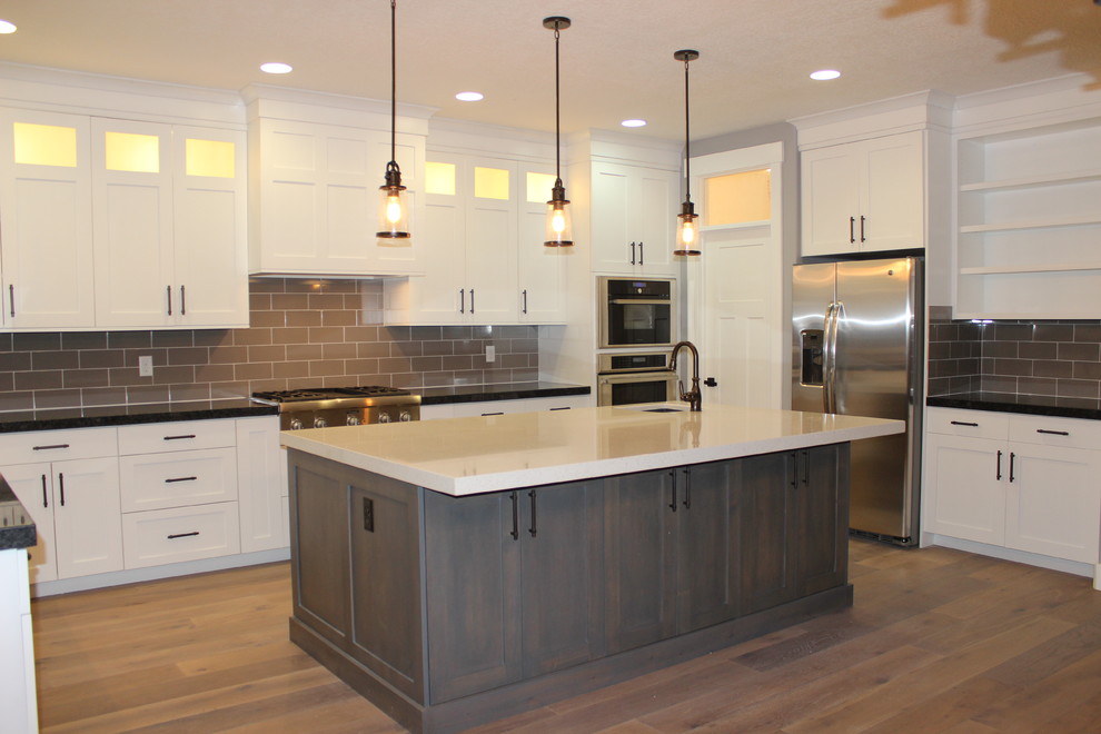 Photo of a large arts and crafts galley eat-in kitchen in Salt Lake City with an undermount sink, raised-panel cabinets, white cabinets, granite benchtops, grey splashback, ceramic splashback, stainless steel appliances, medium hardwood floors and with island.