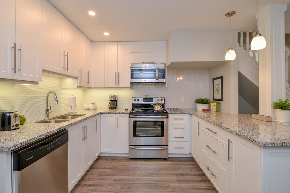 Example of a mid-sized transitional u-shaped medium tone wood floor and gray floor open concept kitchen design with an undermount sink, shaker cabinets, white cabinets, granite countertops, stainless steel appliances and a peninsula