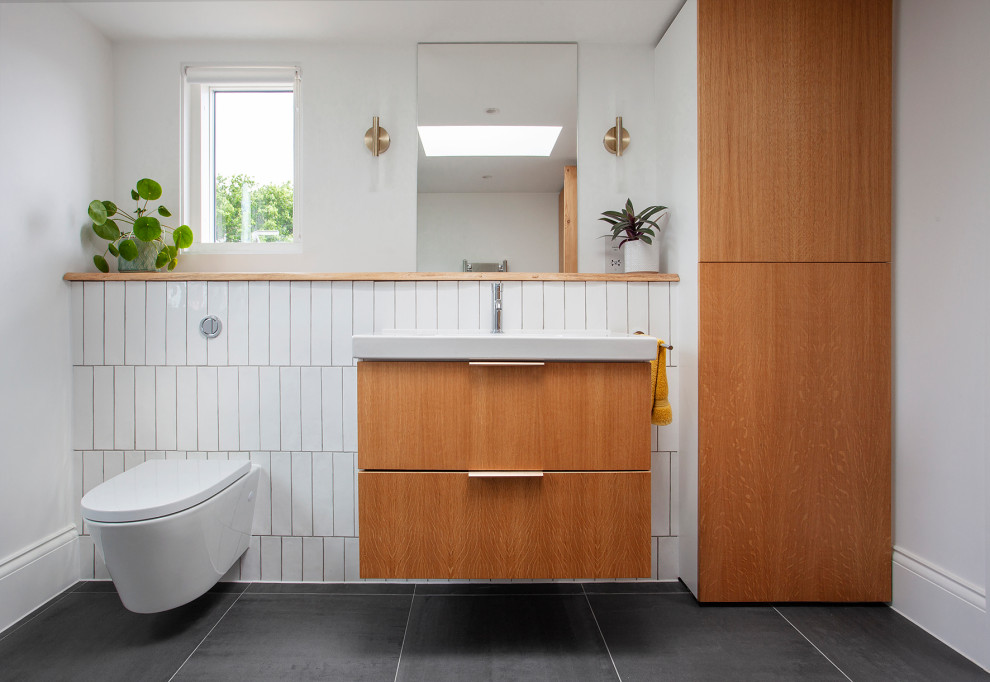 Small midcentury 3/4 bathroom in London with flat-panel cabinets, light wood cabinets, a curbless shower, a wall-mount toilet, white tile, ceramic tile, white walls, ceramic floors, a console sink, wood benchtops, grey floor, a hinged shower door, brown benchtops, a single vanity and a floating vanity.