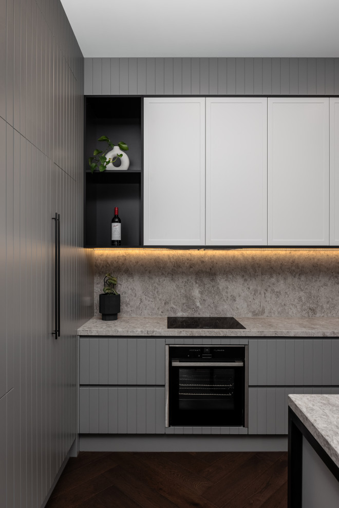 This is an example of a large contemporary galley kitchen pantry in Melbourne with a drop-in sink, flat-panel cabinets, grey cabinets, marble benchtops, white splashback, marble splashback, black appliances, dark hardwood floors, with island, brown floor and white benchtop.