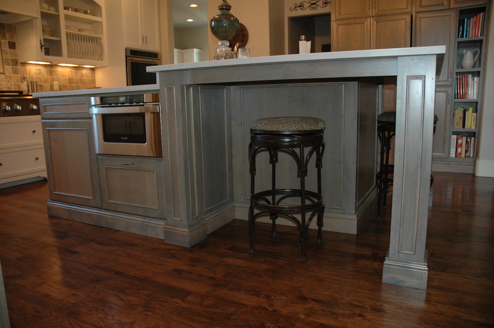 Large transitional u-shaped medium tone wood floor kitchen pantry photo with a farmhouse sink, flat-panel cabinets, white cabinets, granite countertops, brown backsplash, stone tile backsplash, paneled appliances and an island