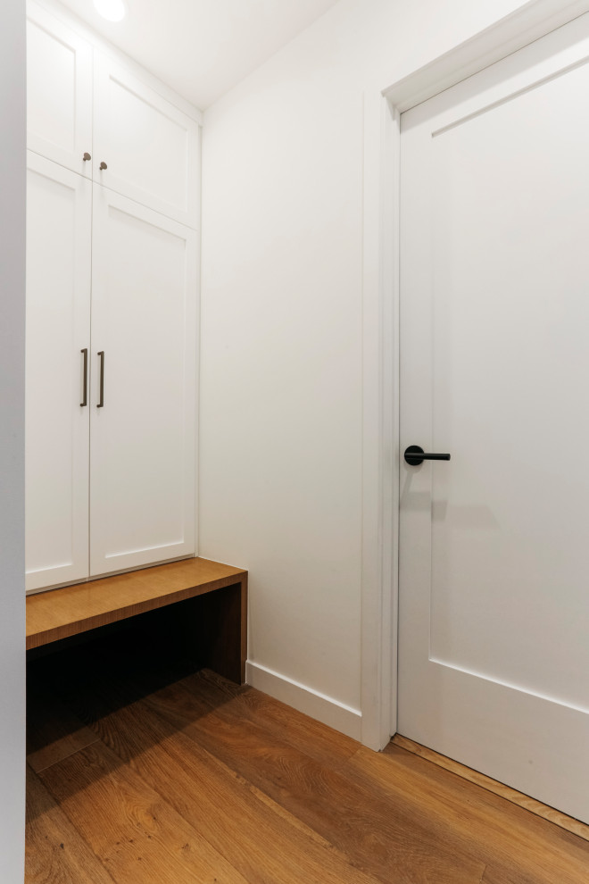 60 tals inredning av en entré, med vita väggar, mellanmörkt trägolv, en enkeldörr, en vit dörr och brunt golv