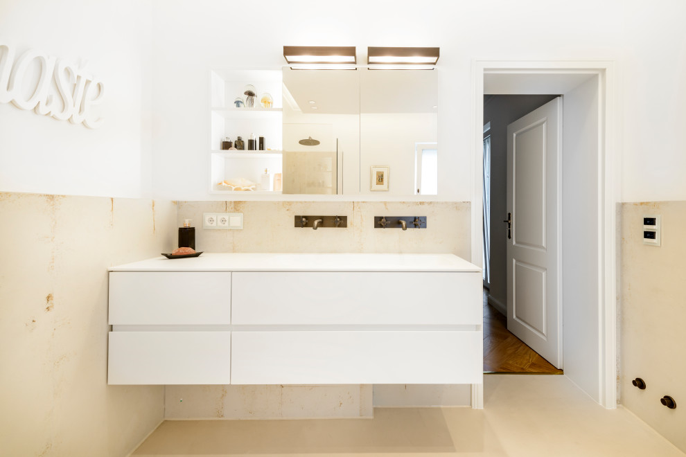 Photo of a mid-sized traditional bathroom in Cologne with a freestanding tub, beige tile, beige floor, flat-panel cabinets, white cabinets, an open shower, a wall-mount toilet, ceramic tile, beige walls, an integrated sink, solid surface benchtops, an open shower and white benchtops.