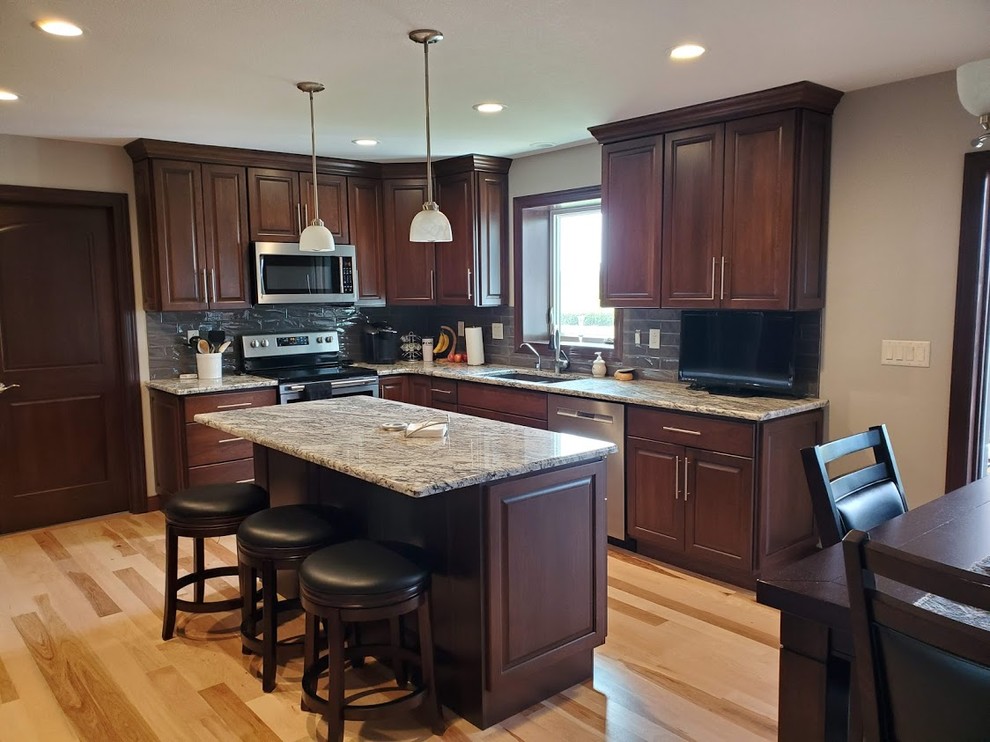 Example of a large transitional u-shaped light wood floor and multicolored floor eat-in kitchen design in Cedar Rapids with an undermount sink, raised-panel cabinets, dark wood cabinets, granite countertops, metallic backsplash, ceramic backsplash, stainless steel appliances, an island and gray countertops