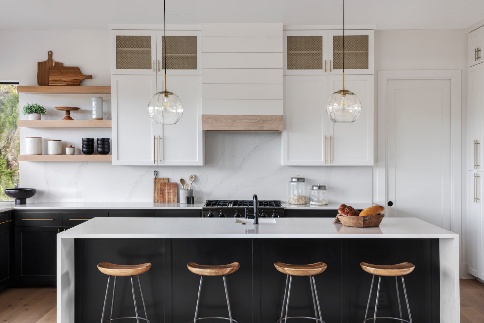 Inspiration for a mid-sized country u-shaped eat-in kitchen in Austin with a farmhouse sink, shaker cabinets, black cabinets, quartz benchtops, white splashback, engineered quartz splashback, stainless steel appliances, light hardwood floors, with island, brown floor, white benchtop and timber.