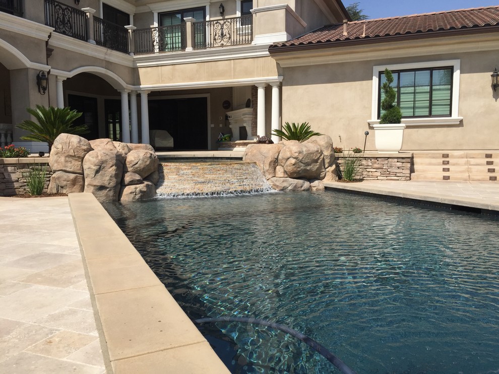 Large traditional backyard custom-shaped pool in Los Angeles with a water feature and natural stone pavers.