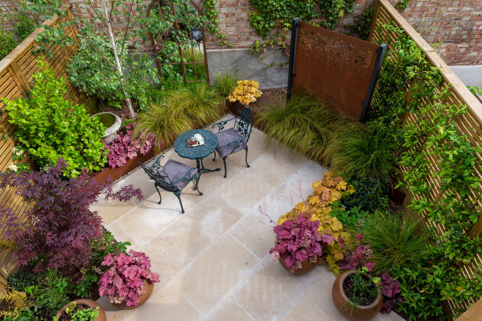 Small contemporary courtyard partial sun xeriscape in London with with raised garden bed, natural stone pavers and a wood fence for summer.