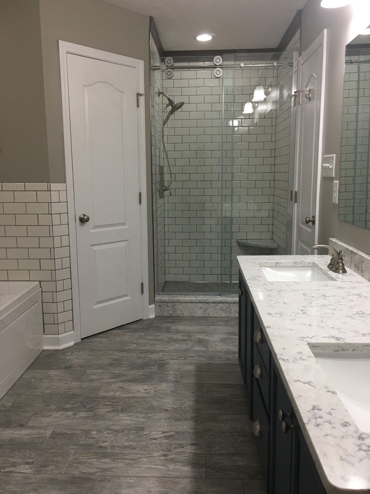 This is an example of a mid-sized contemporary master bathroom in Raleigh with beaded inset cabinets, blue cabinets, a hot tub, an alcove shower, a one-piece toilet, gray tile, porcelain tile, grey walls, ceramic floors, an undermount sink, quartzite benchtops, multi-coloured floor, a sliding shower screen and white benchtops.