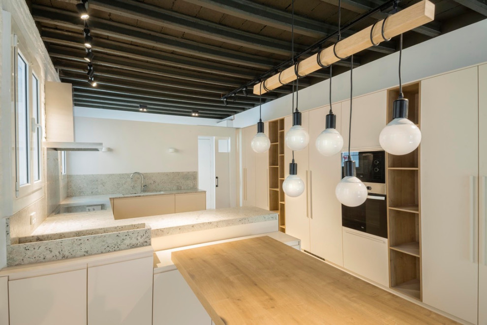 This is an example of a mid-sized industrial u-shaped open plan kitchen in Barcelona with an undermount sink, beige cabinets, quartz benchtops, multi-coloured splashback, black appliances, concrete floors, no island, beige floor and multi-coloured benchtop.