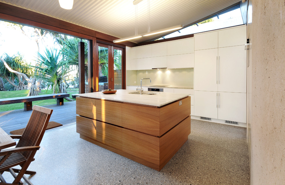 This is an example of a mid-sized contemporary galley kitchen in Sunshine Coast with an undermount sink, flat-panel cabinets, white cabinets, white splashback, panelled appliances, with island, grey floor and concrete floors.