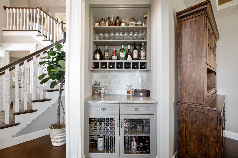 Photo of a small transitional single-wall home bar in Portland with no sink, recessed-panel cabinets, grey cabinets, granite benchtops, grey splashback, porcelain splashback, dark hardwood floors and grey benchtop.