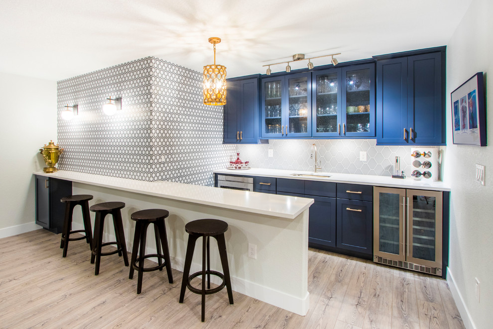 This is an example of a transitional single-wall seated home bar in Denver with an undermount sink, shaker cabinets, blue cabinets, grey splashback, medium hardwood floors, brown floor and white benchtop.