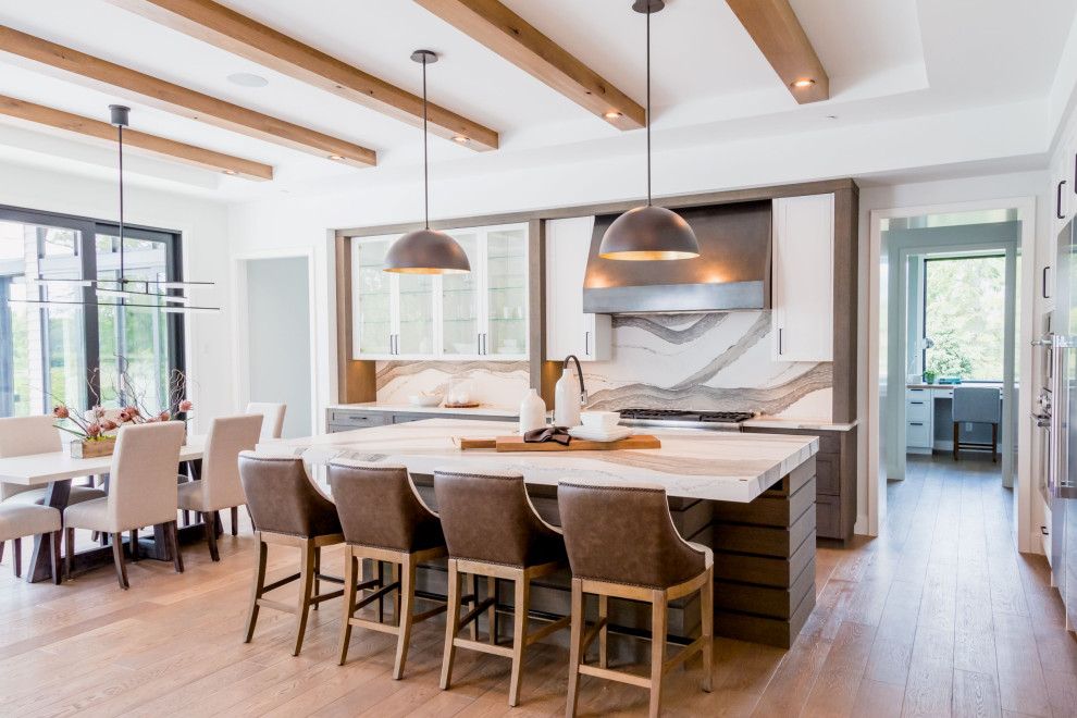 Photo of a large modern l-shaped eat-in kitchen in Minneapolis with recessed-panel cabinets, medium wood cabinets, quartz benchtops, white splashback, engineered quartz splashback, stainless steel appliances, light hardwood floors, with island, brown floor, white benchtop and exposed beam.