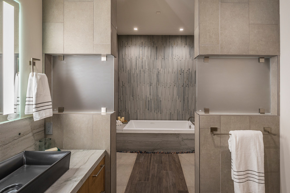 This is an example of an expansive modern master bathroom in Sacramento with flat-panel cabinets, brown cabinets, a drop-in tub, a curbless shower, a two-piece toilet, gray tile, porcelain tile, white walls, porcelain floors, a vessel sink, quartzite benchtops, beige floor and a hinged shower door.