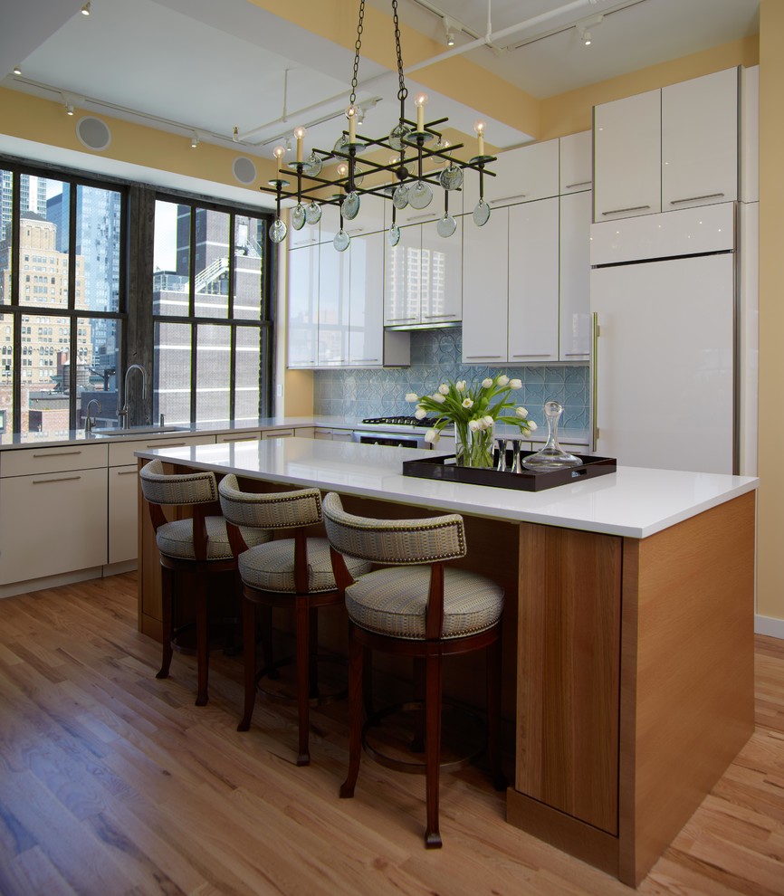 This is an example of a contemporary l-shaped kitchen in New York with flat-panel cabinets, white cabinets, blue splashback, panelled appliances, light hardwood floors and with island.