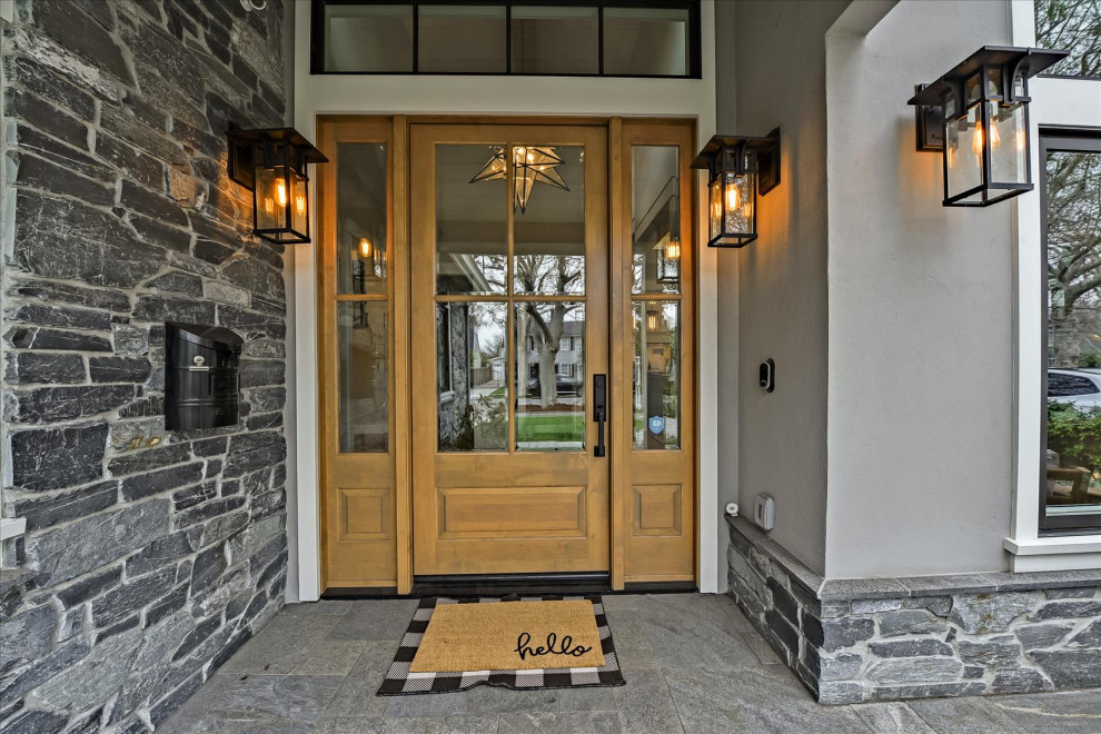 Cette photo montre un grand porche d'entrée de maison avant craftsman avec des pavés en pierre naturelle et une extension de toiture.