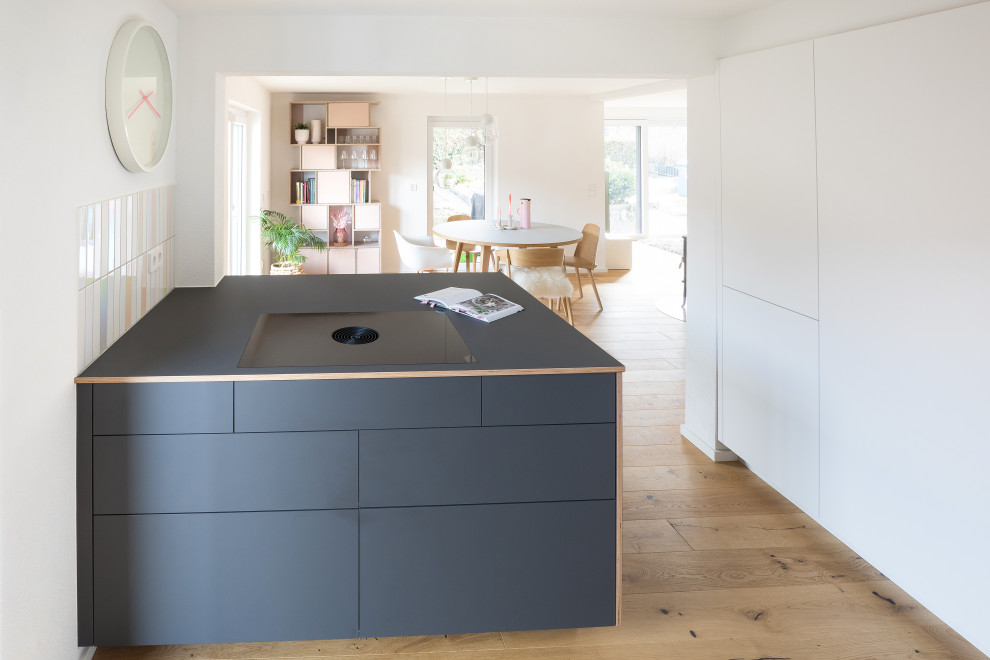 Example of a mid-sized danish l-shaped open concept kitchen design in Stuttgart with white cabinets, wood countertops, porcelain backsplash, an island and black countertops