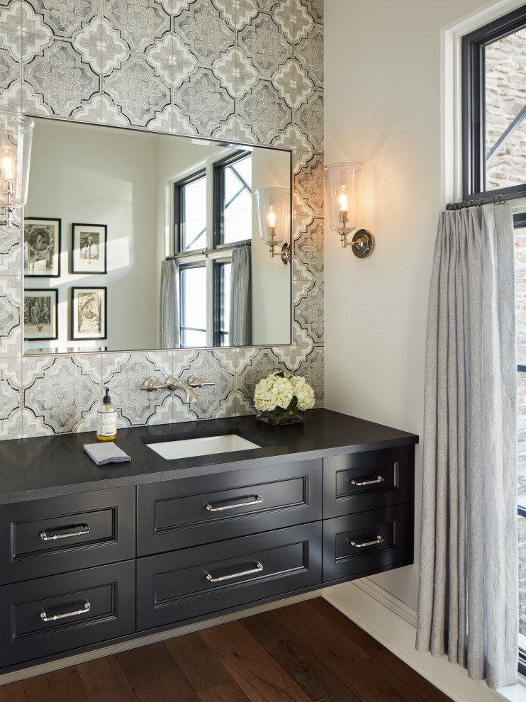 This is an example of a large transitional powder room in Chicago with flat-panel cabinets, black cabinets, multi-coloured tile, ceramic tile, white walls, medium hardwood floors, an undermount sink, granite benchtops, brown floor and black benchtops.
