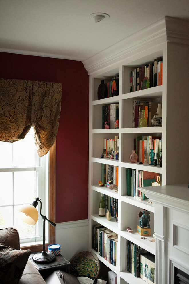 This is an example of a traditional enclosed family room in Portland Maine with a library, red walls, medium hardwood floors, a standard fireplace and a wood fireplace surround.