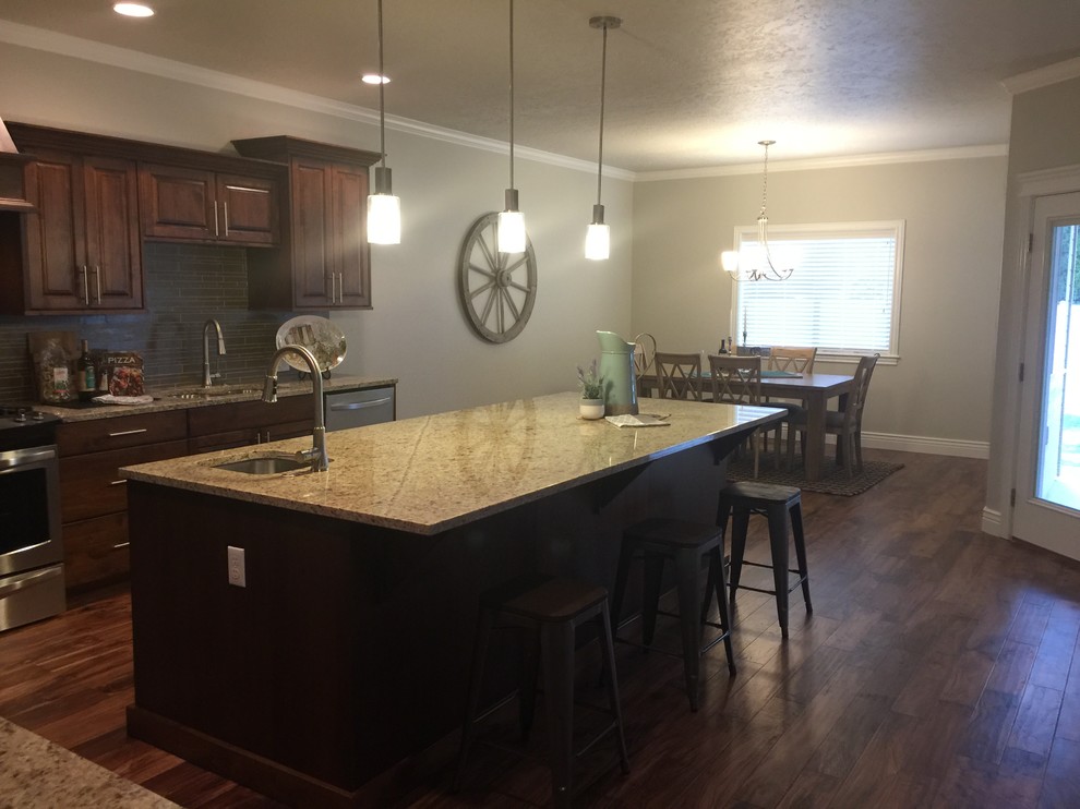 Open concept kitchen - mid-sized rustic l-shaped dark wood floor open concept kitchen idea in Boise with an undermount sink, raised-panel cabinets, dark wood cabinets, granite countertops, gray backsplash, glass tile backsplash, stainless steel appliances and an island