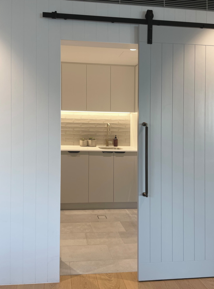 This is an example of a mid-sized contemporary l-shaped dedicated laundry room in Sydney with an undermount sink, concrete benchtops, grey splashback, ceramic splashback, white walls, limestone floors, a stacked washer and dryer, grey floor and grey benchtop.