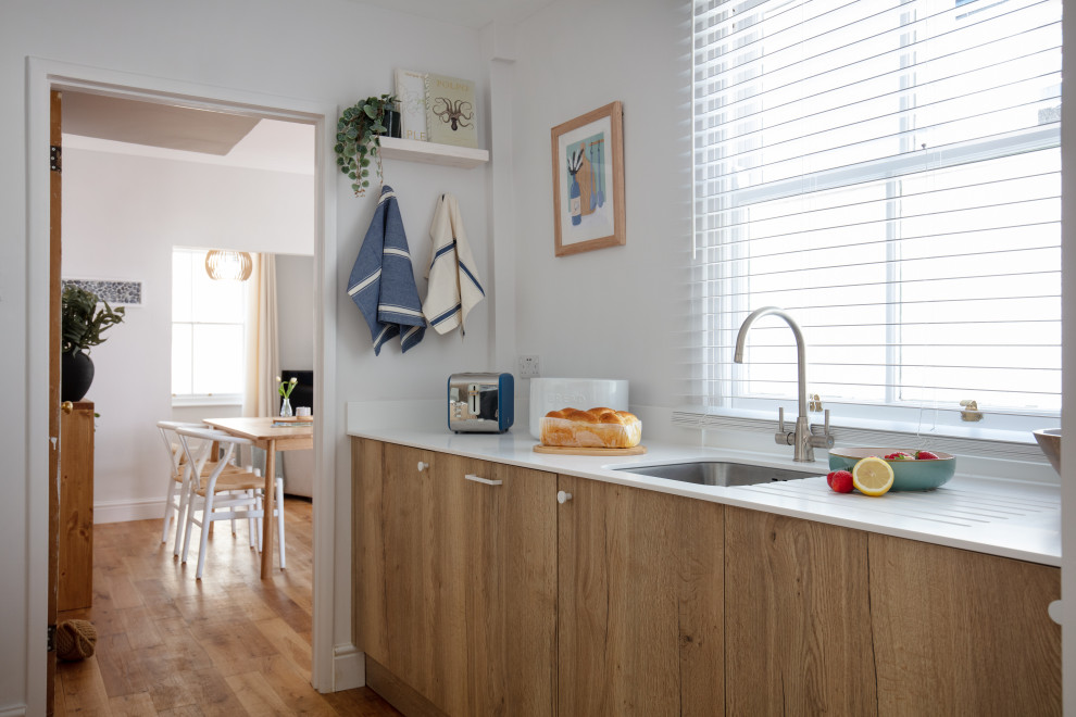 This is an example of a small scandinavian galley separate kitchen in Cornwall with a single-bowl sink, flat-panel cabinets, medium wood cabinets, solid surface benchtops, white splashback, subway tile splashback, medium hardwood floors, no island, brown floor and white benchtop.