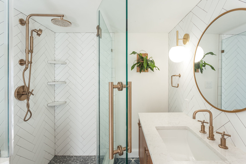 This is an example of a mid-sized midcentury 3/4 bathroom in DC Metro with flat-panel cabinets, medium wood cabinets, a corner shower, a two-piece toilet, white tile, subway tile, white walls, cement tiles, an undermount sink, engineered quartz benchtops, blue floor, a hinged shower door, white benchtops and brick walls.