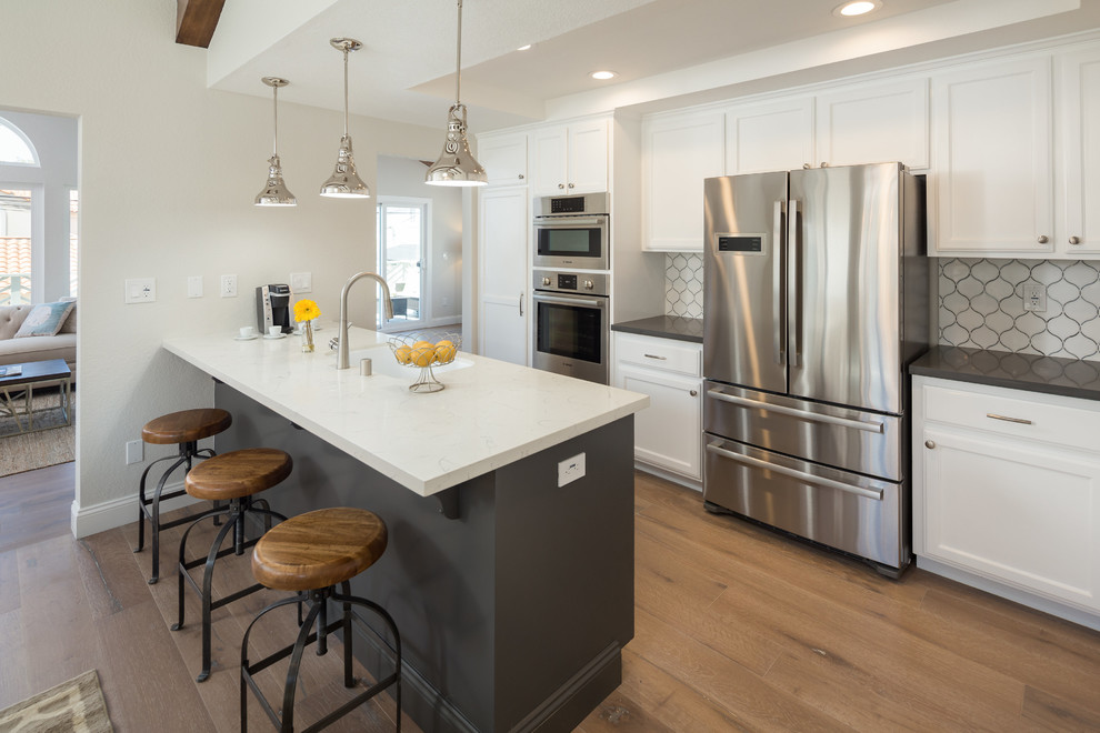 Transitional eat-in kitchen in Los Angeles with an undermount sink, quartz benchtops, white splashback, stainless steel appliances and a peninsula.
