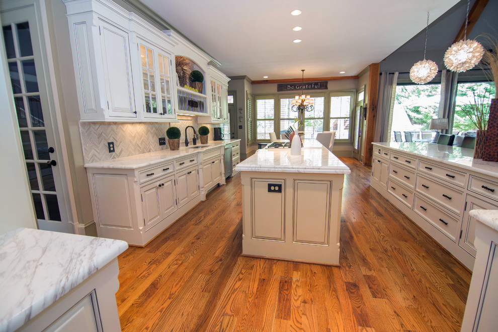 Photo of a mid-sized traditional u-shaped eat-in kitchen in Atlanta with a drop-in sink, recessed-panel cabinets, white cabinets, marble benchtops, white splashback, stone tile splashback, stainless steel appliances, medium hardwood floors and with island.