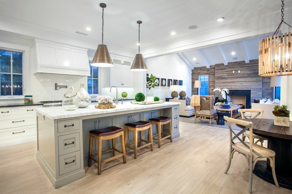 Photo of an eclectic open plan kitchen in Orange County with grey cabinets, marble benchtops, white splashback, glass tile splashback, stainless steel appliances, light hardwood floors and with island.