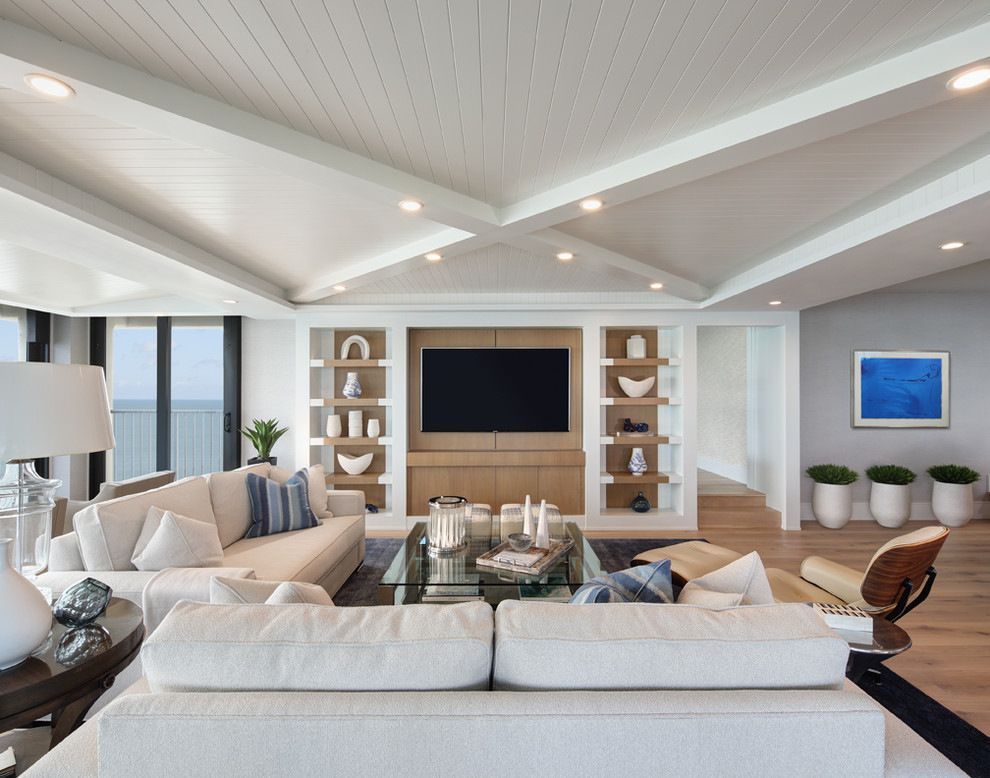 Inspiration for a beach style open concept family room in Miami with grey walls, medium hardwood floors, a wall-mounted tv and brown floor.