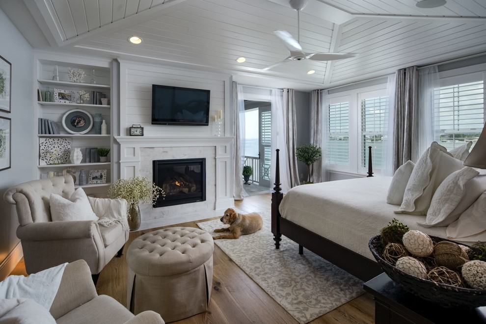 Large beach style master bedroom in Tampa with grey walls, light hardwood floors, a standard fireplace, a stone fireplace surround and brown floor.