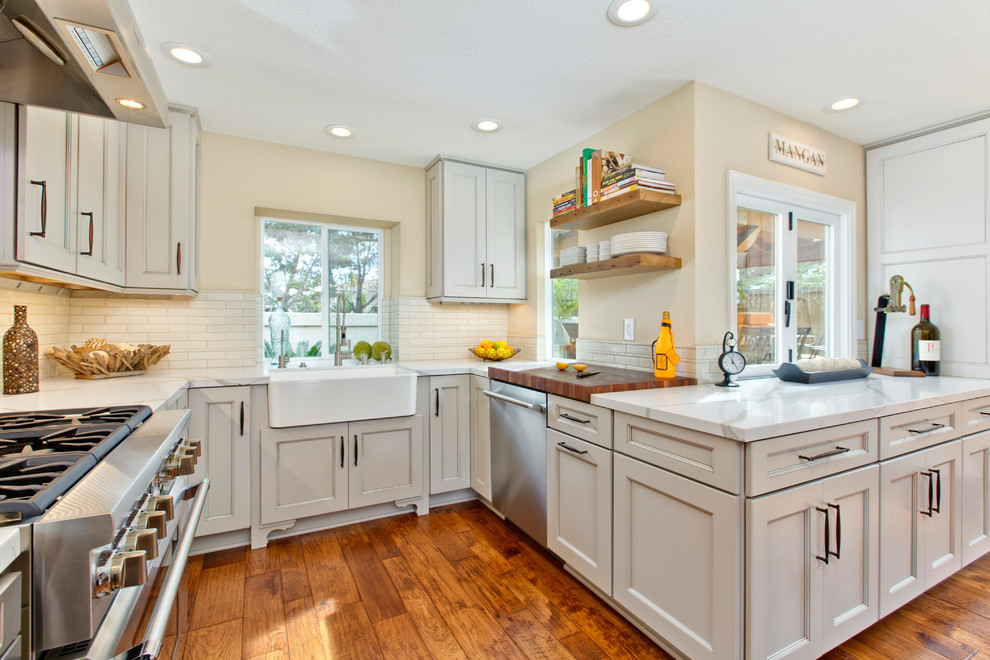 Inspiration for a mid-sized traditional u-shaped open plan kitchen in Tampa with a farmhouse sink, recessed-panel cabinets, grey cabinets, quartzite benchtops, beige splashback, porcelain splashback, stainless steel appliances, medium hardwood floors and no island.