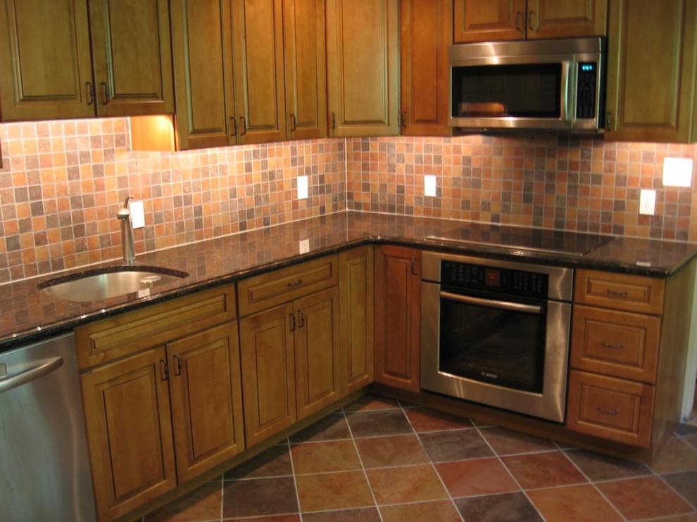 This is an example of a mid-sized traditional l-shaped eat-in kitchen in Philadelphia with medium wood cabinets, brown splashback, stainless steel appliances, no island, an undermount sink, raised-panel cabinets, granite benchtops, terra-cotta splashback, terra-cotta floors and brown floor.