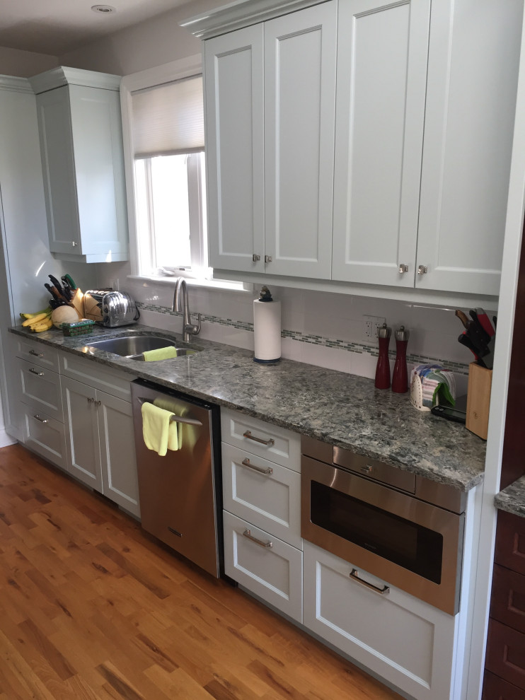 Example of a mid-sized transitional galley medium tone wood floor and brown floor enclosed kitchen design in Ottawa with a double-bowl sink, recessed-panel cabinets, gray cabinets, granite countertops, porcelain backsplash, stainless steel appliances and gray countertops